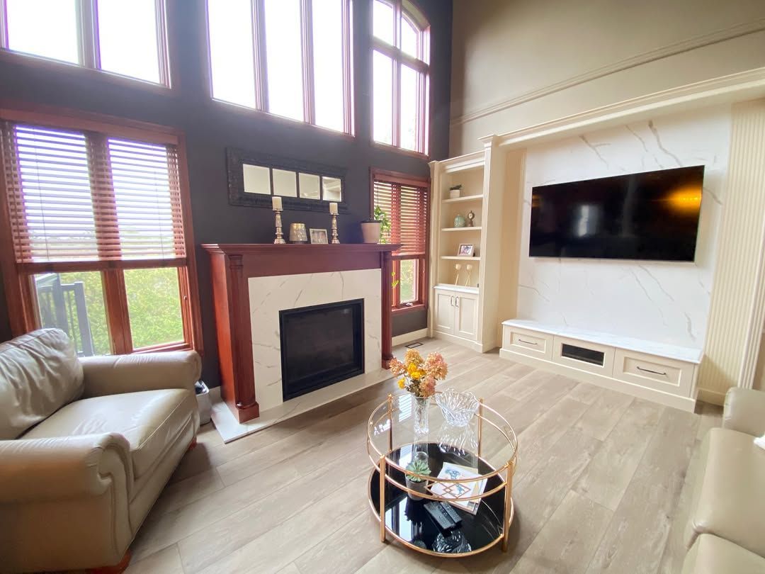 Living room with fireplace, TV, and tan furniture. Windows with blinds let in sunlight.
