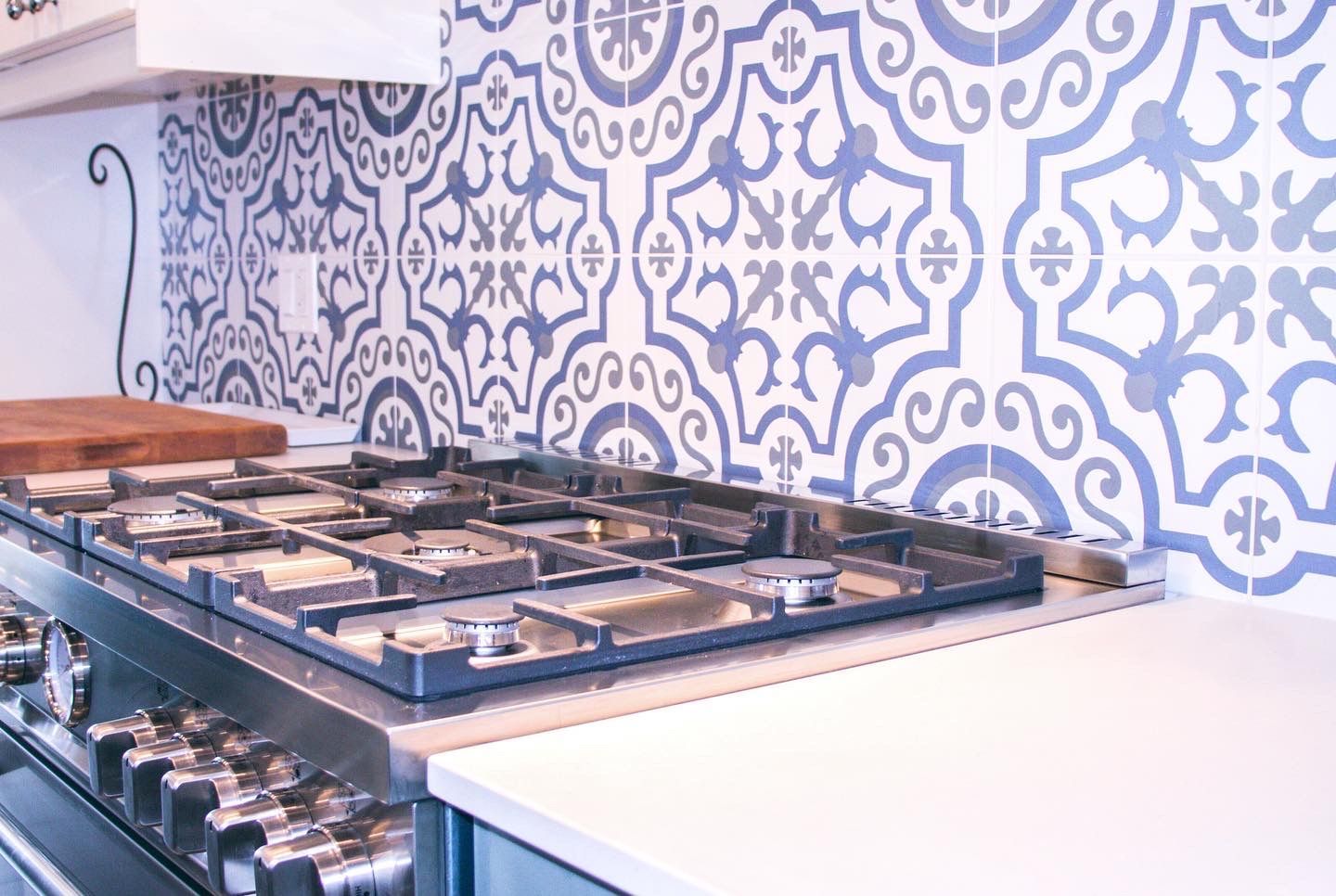 Stainless steel gas range with blue and white patterned tile backsplash.
