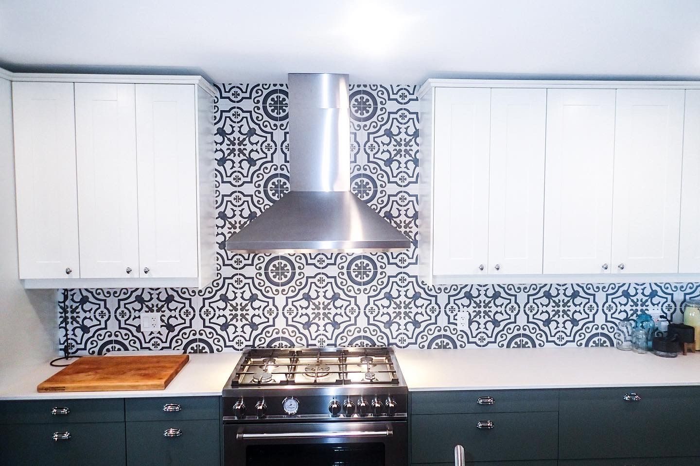 Kitchen with white cabinets, patterned backsplash, stainless steel hood over dark stove.