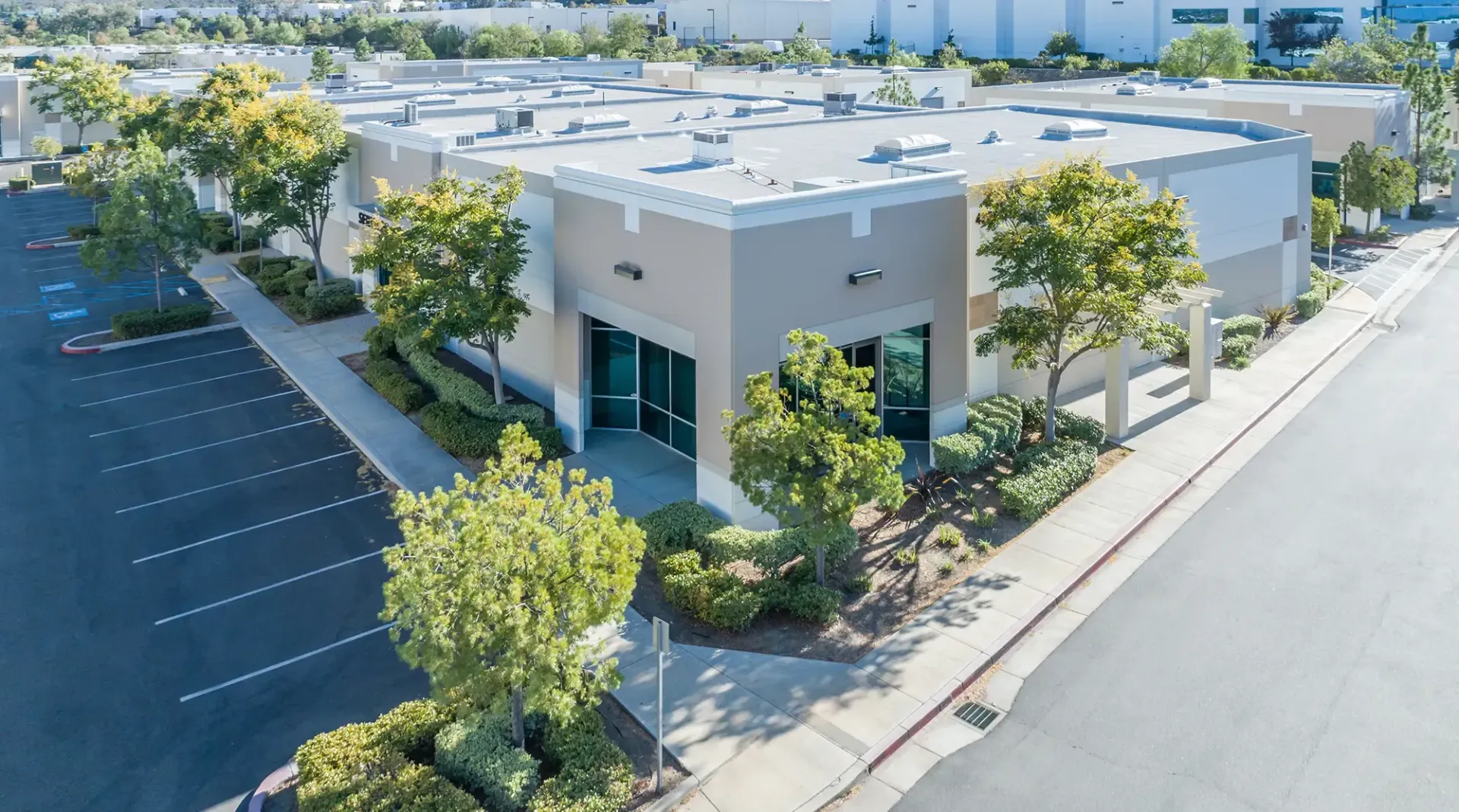 Exterior view of a beige commercial building with a parking lot. Trees and blue sky.