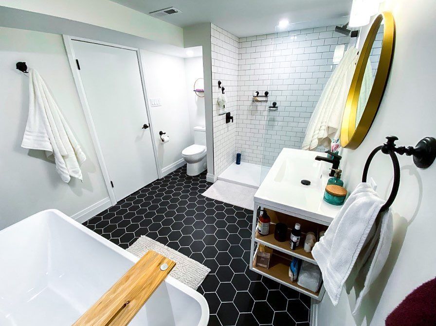 Modern bathroom with black hexagon tile floor, white walls, tub, and shower. Gold mirror and fixtures.