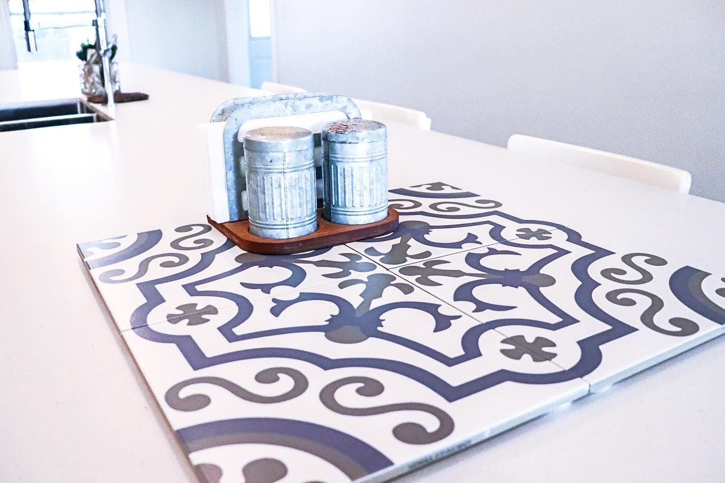 Salt and pepper shakers, napkin holder on decorative tile, on white table.