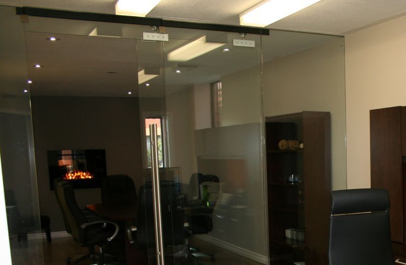 Glass office sliding door, partially frosted, separates two rooms with office furniture and a TV.