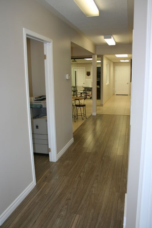 Hallway with wood-look floor, beige walls, and doorways leading to offices and a room with equipment.