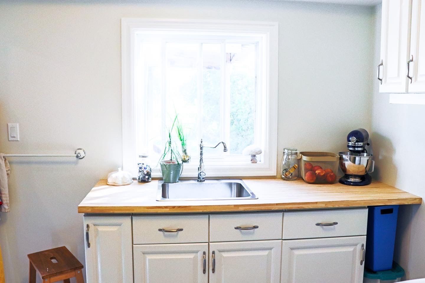 Kitchen with white cabinets, wooden countertop, sink under a window, and a stand mixer.
