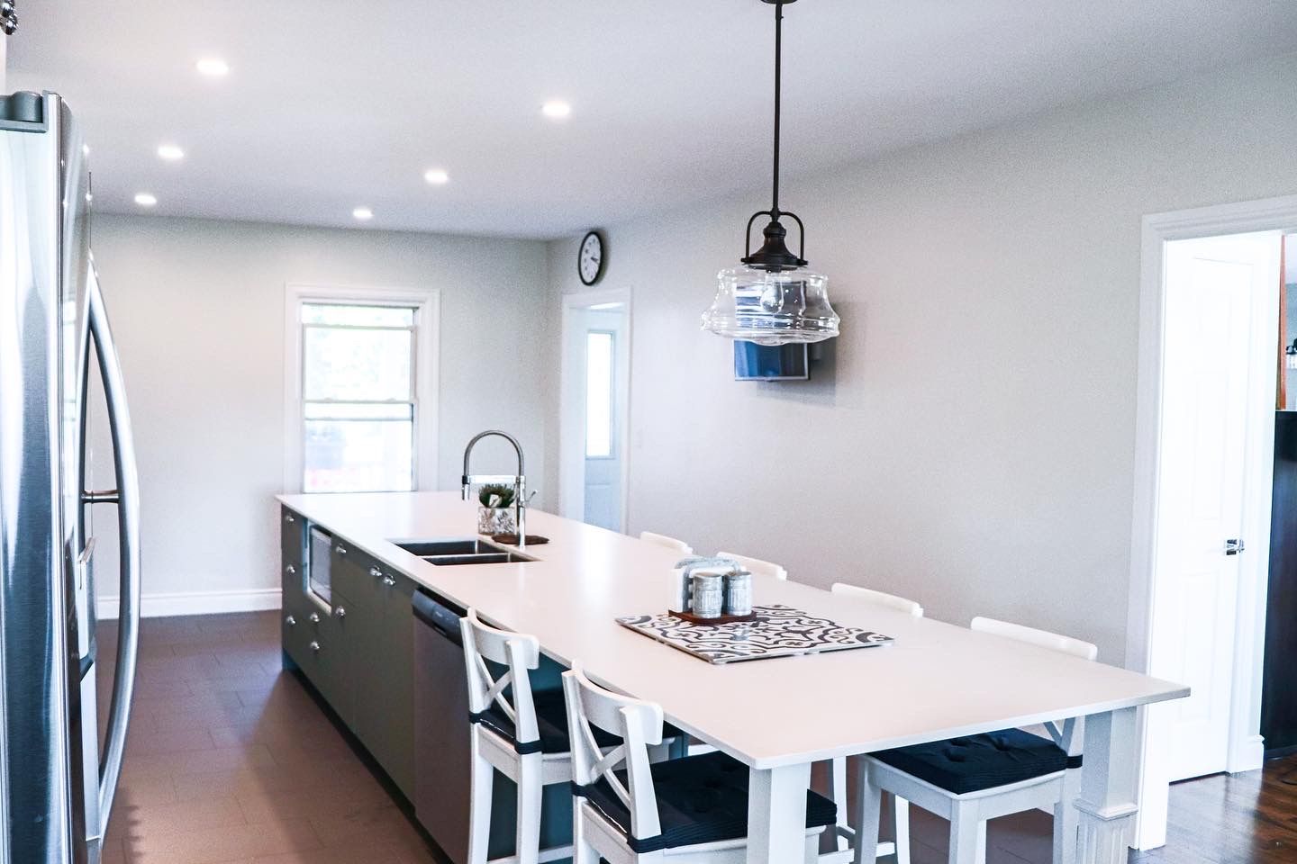 Spacious kitchen with a large island, stainless steel appliances, white walls, and pendant light.