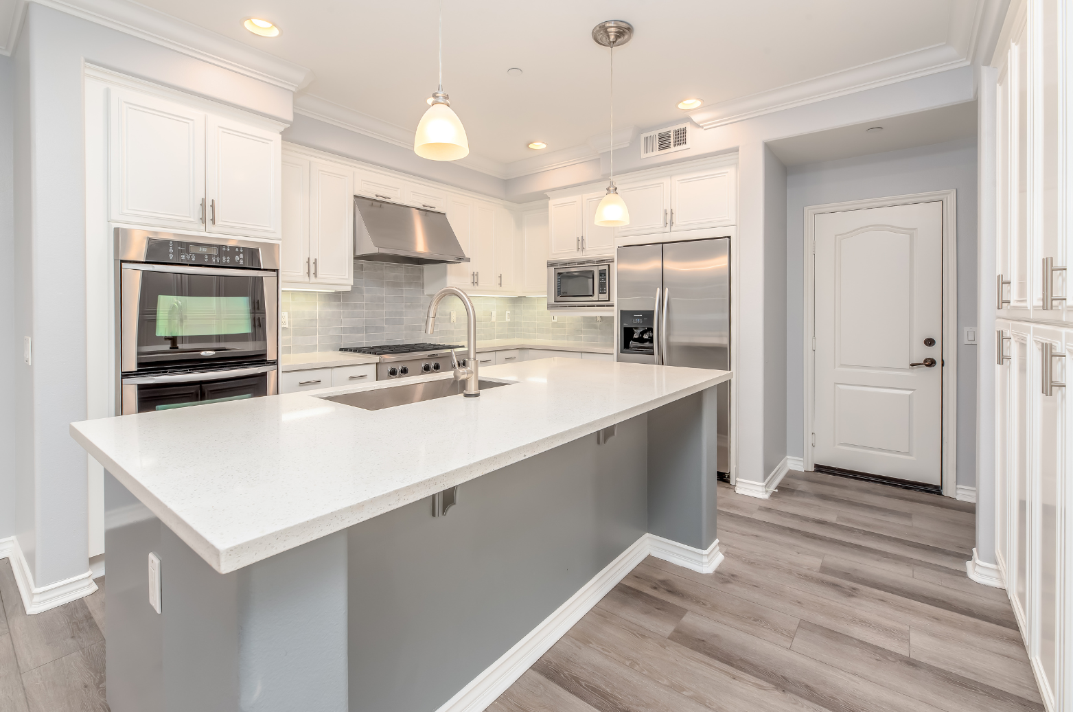 Modern white kitchen with stainless steel appliances, gray island, and light wood floors.