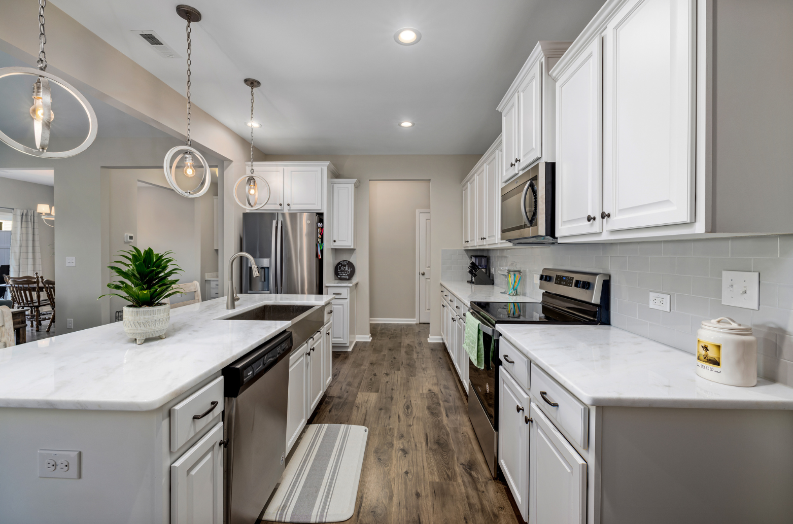White kitchen with island, stainless steel appliances, wood floor, and white cabinets.