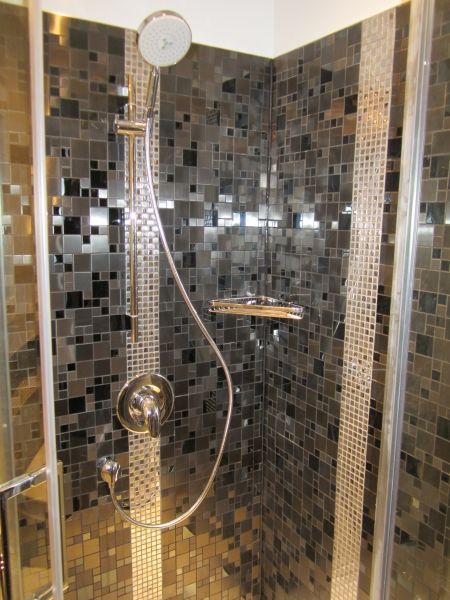Shower with black and silver mosaic tile, chrome fixtures, and glass door.