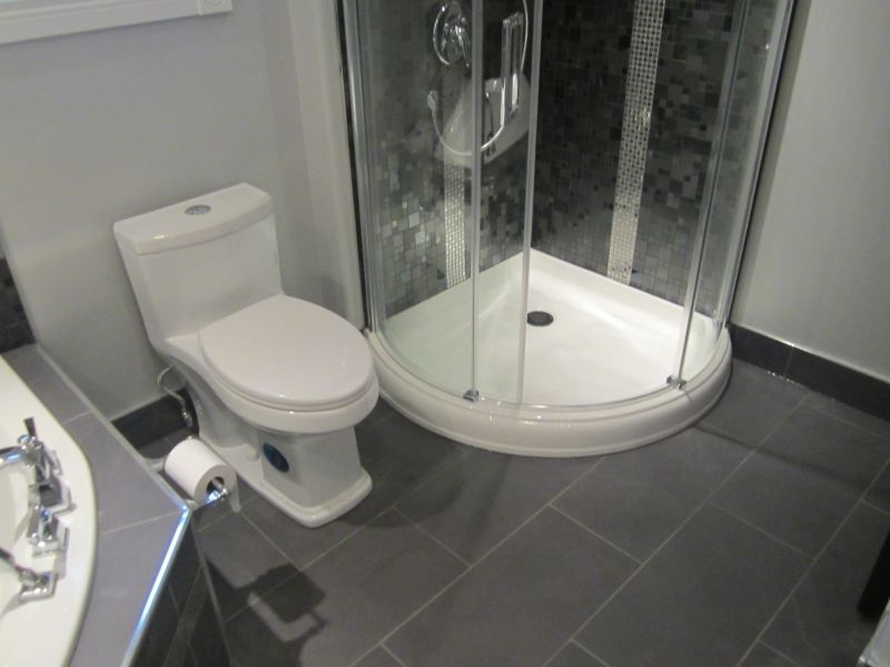 Bathroom with a white toilet, a glass shower, and gray tile flooring.