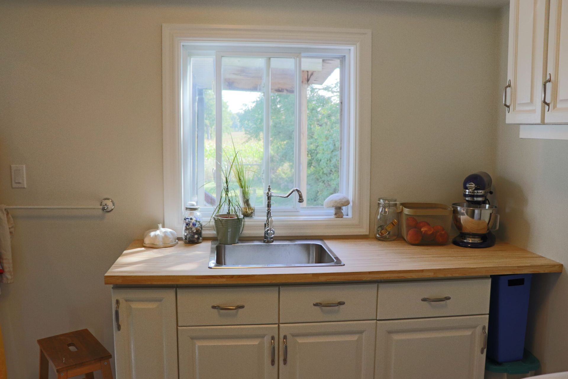 Kitchen with a sink, window, wooden countertop, white cabinets, and a stand mixer.