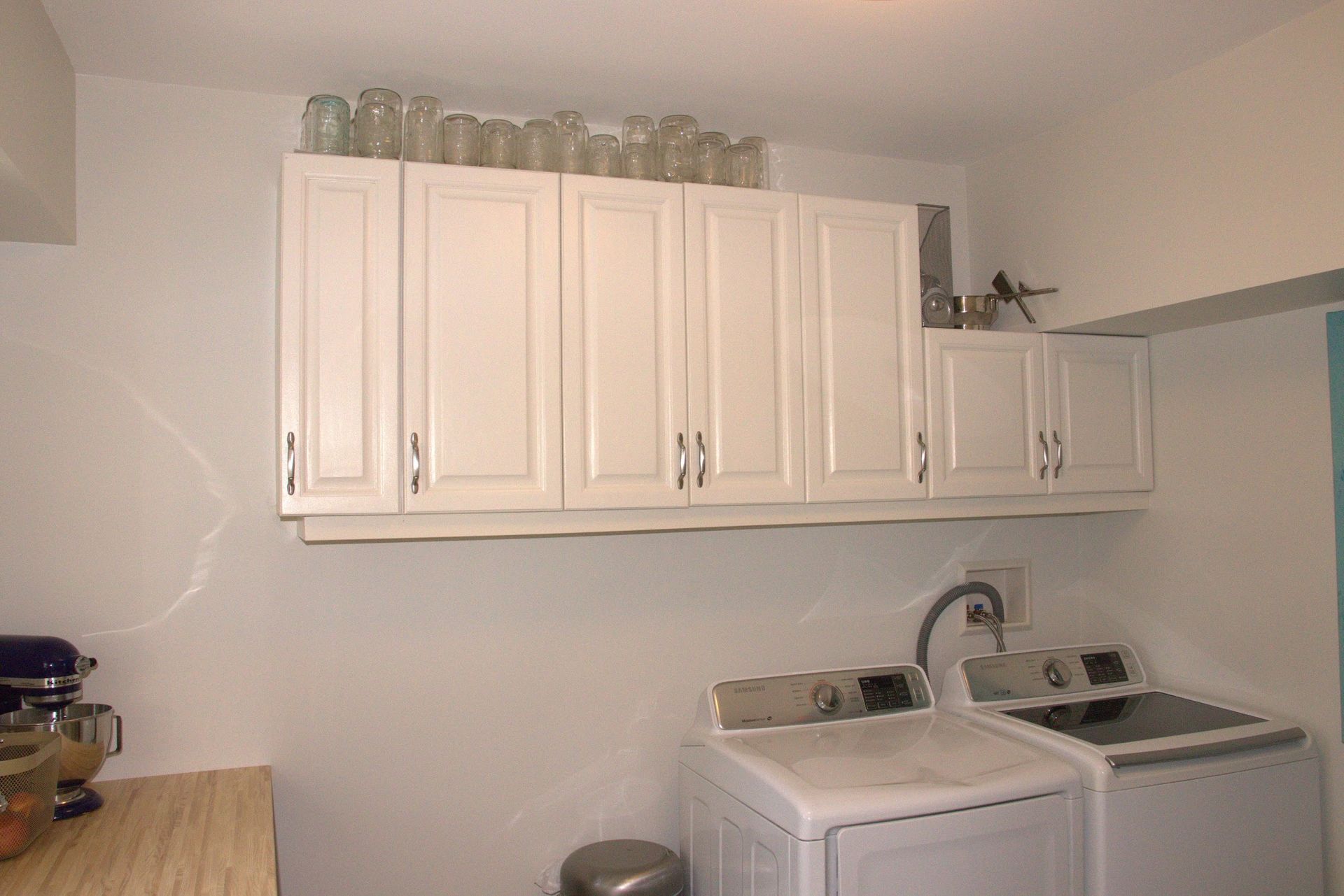 White cabinets above a washer and dryer in a laundry room. Glass jars are on top of the cabinets.