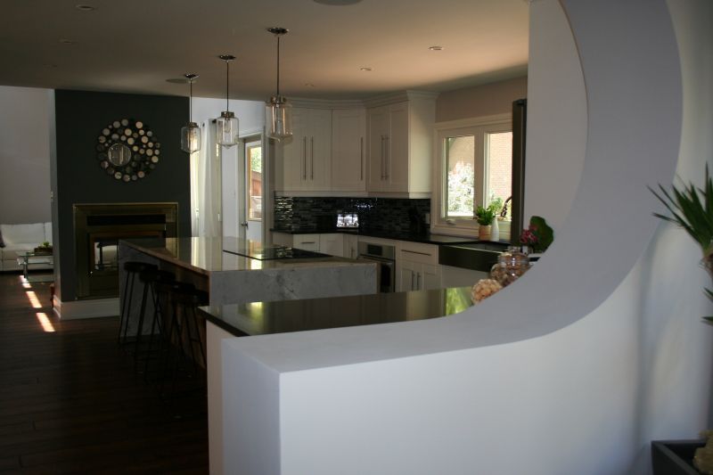 Modern kitchen with white cabinets, black countertops, and a curved white wall divider.