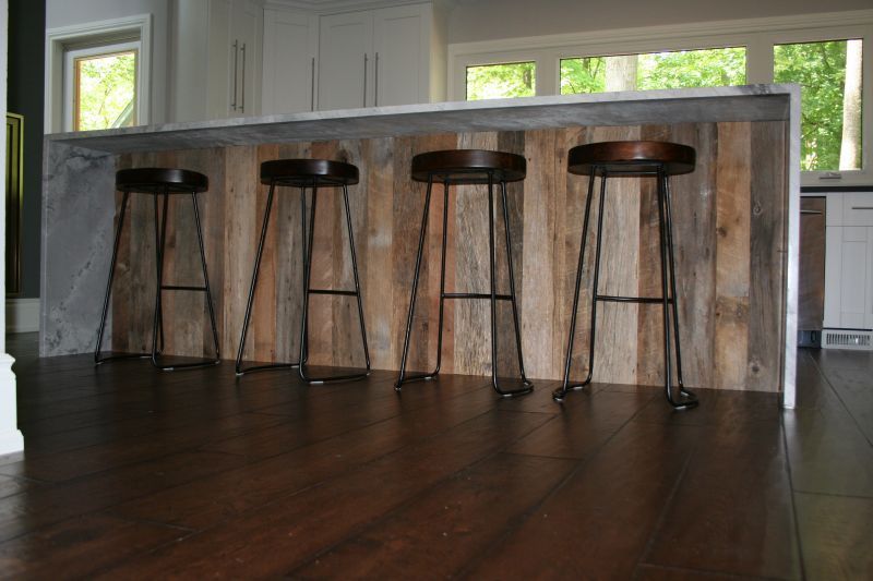 Kitchen island with wooden paneling and four stools on a dark wood floor, with a marble countertop.