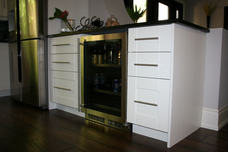 White kitchen cabinets with a stainless steel wine cooler and refrigerator. Dark hardwood floor.