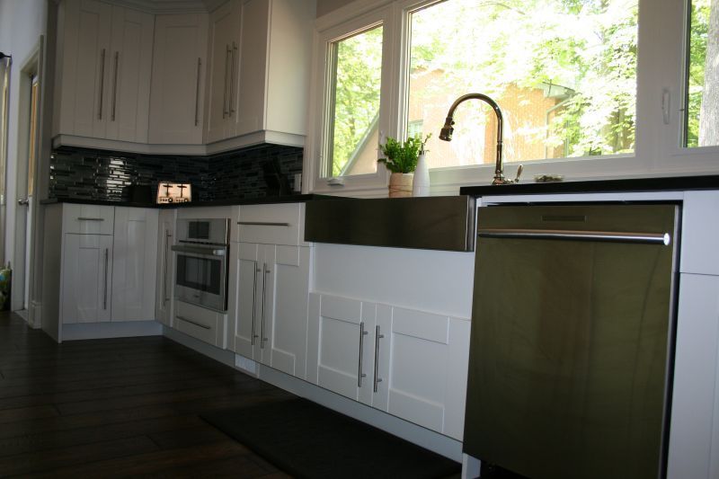 Modern white kitchen with stainless steel sink and appliances, dark countertops, and large window.
