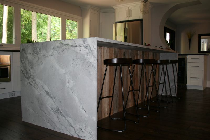 Kitchen island with marble countertop, wood paneling, and bar stools.