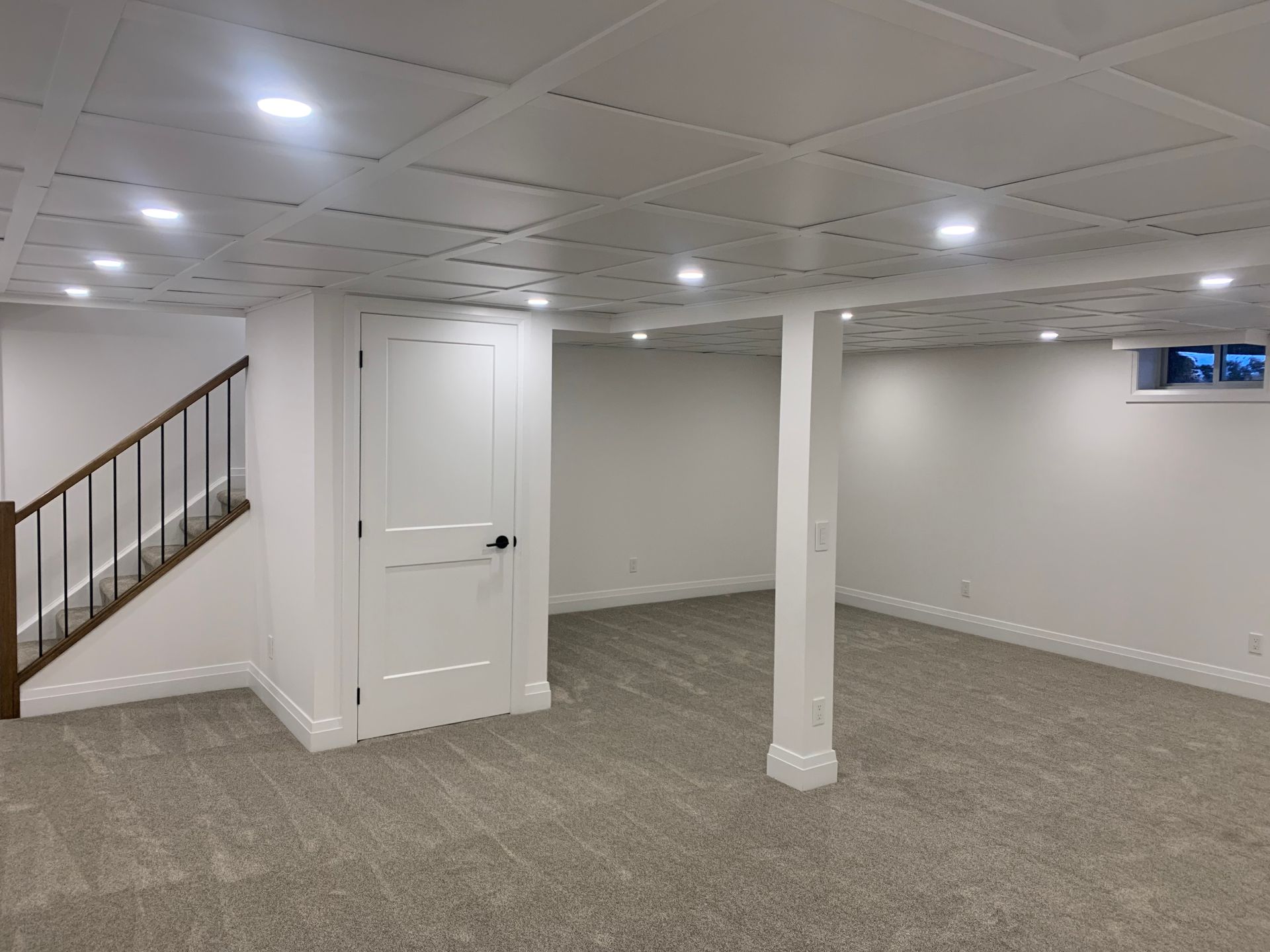 Finished basement with recessed lights, white walls, carpet, stairs, and a door.
