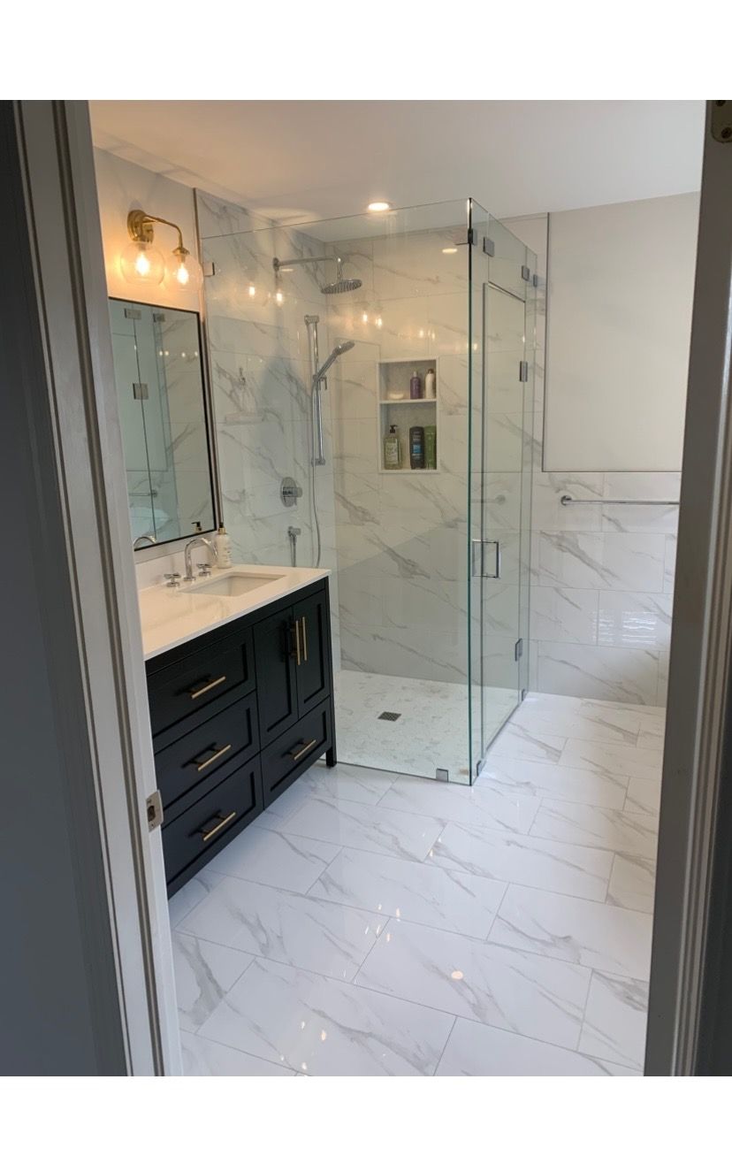 Bathroom with marble-look tiles, glass shower, dark vanity, and gold fixtures.