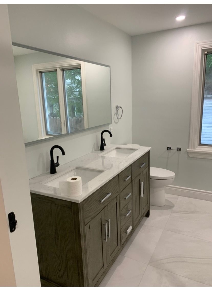 A modern bathroom with a double vanity, black fixtures, and a large mirror.