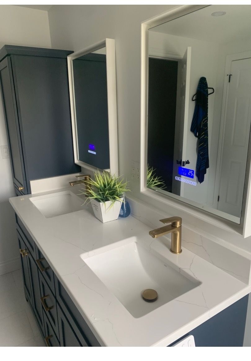 Bathroom vanity with blue cabinets, white countertop, gold fixtures, and large mirrors.
