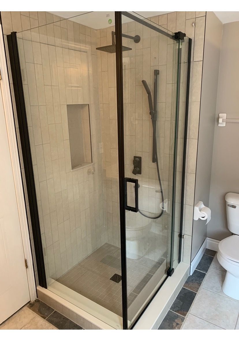 Shower with black frame, clear glass doors. Includes showerhead, handheld, and built-in niche.