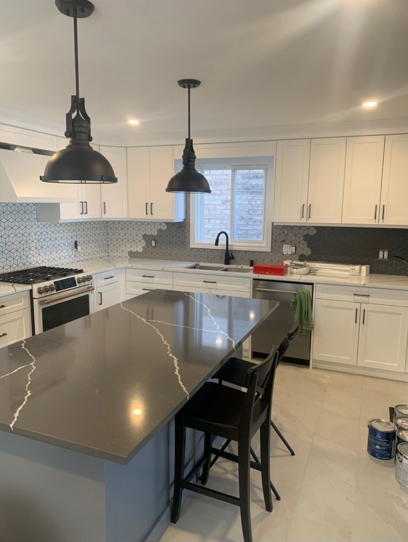 Kitchen with gray island and countertops, white cabinets, and two black pendant lights.