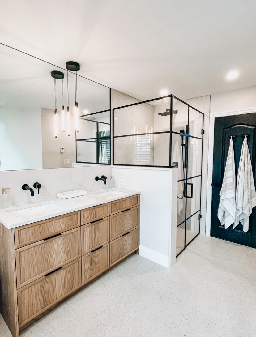Modern bathroom with wood vanity, glass shower, and black fixtures.