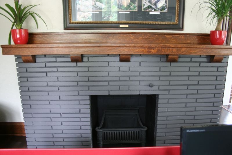 Gray brick fireplace with wooden mantel and two potted plants; a framed picture above.