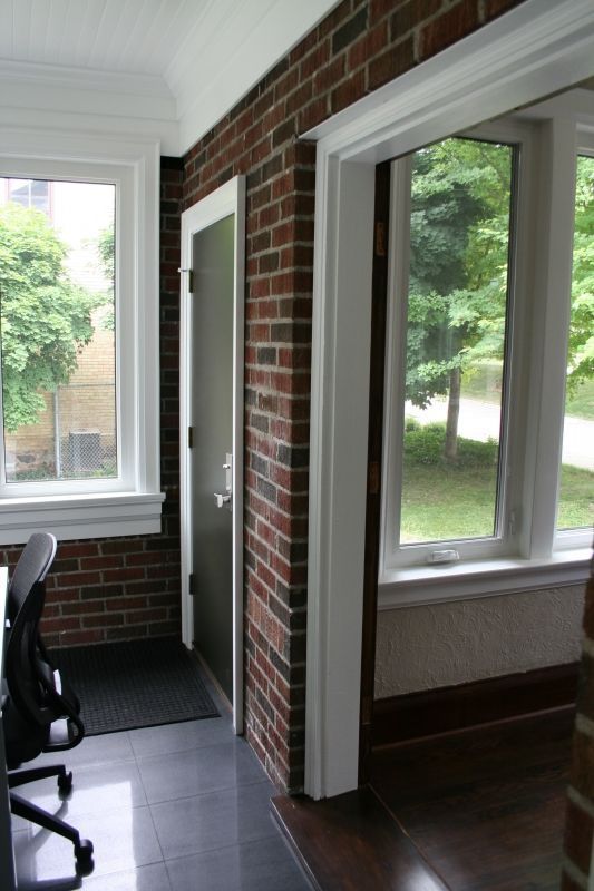 Interior view of a room with brick walls, windows, and a doorway; black chair is in the corner.