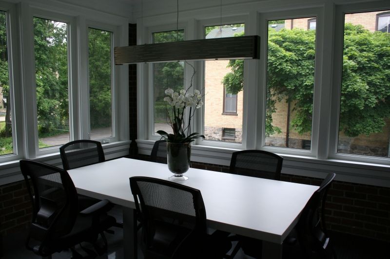 Conference room with large windows overlooking trees, white table, and black chairs.