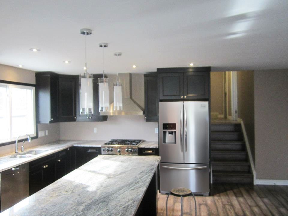 Modern kitchen with black cabinets, stainless steel appliances, and a granite countertop island.