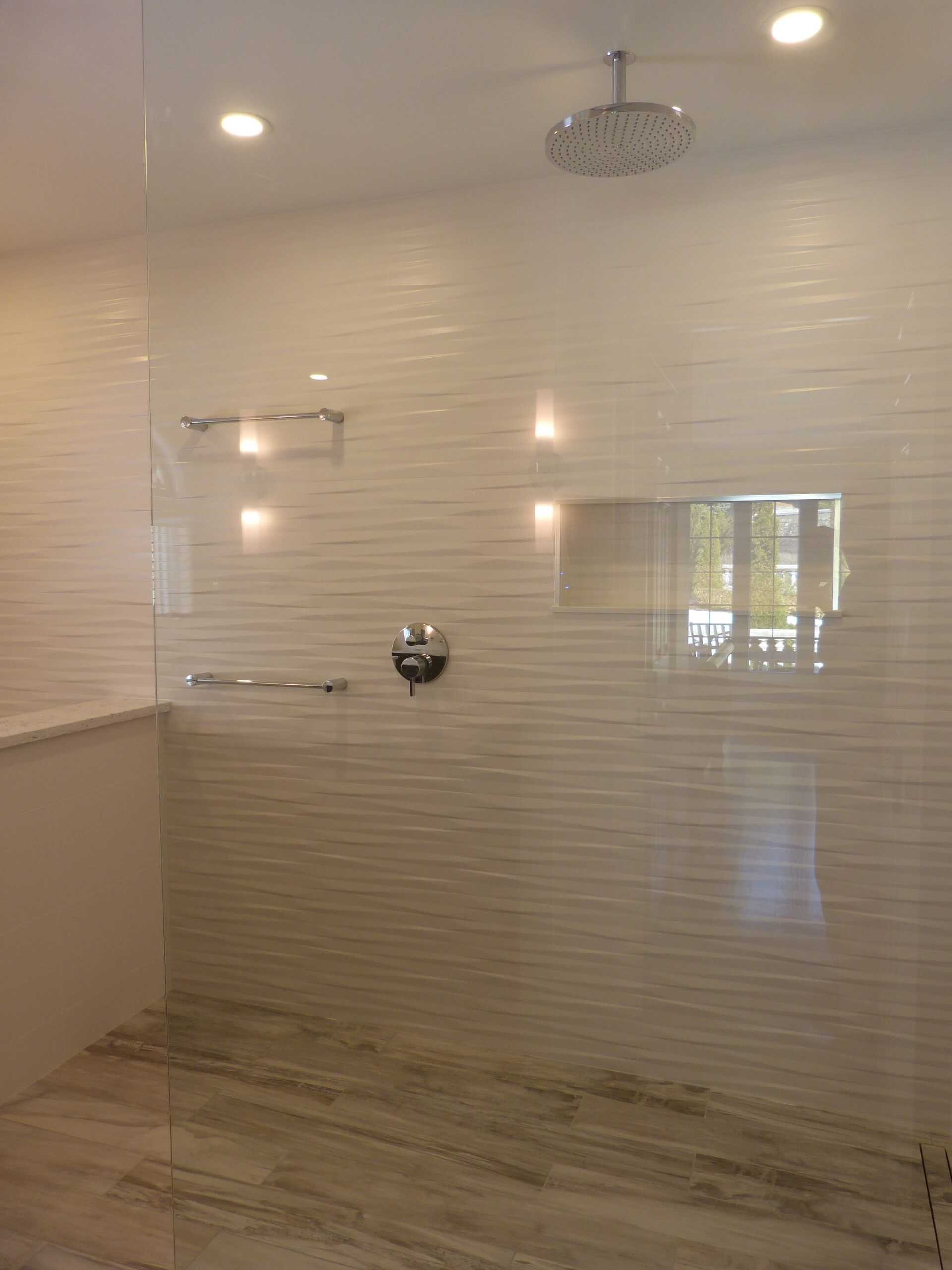 Shower with textured white tile walls, glass enclosure, and stone floor.