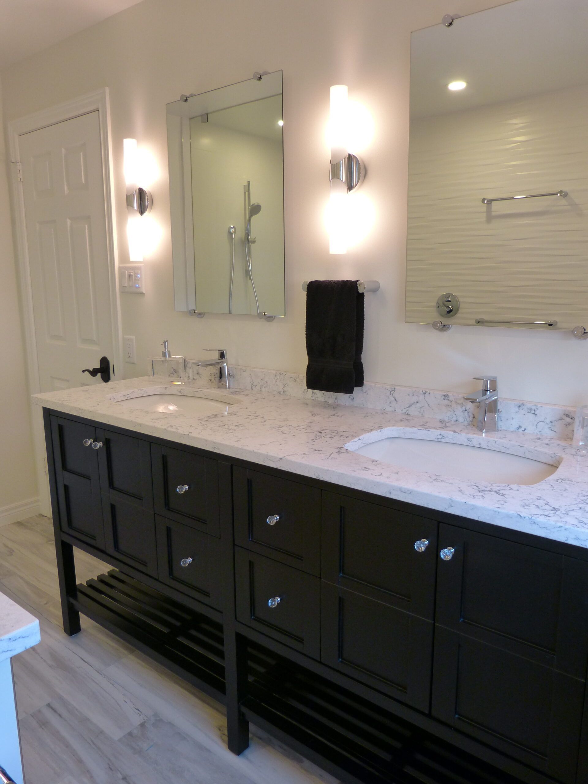 Double sink bathroom vanity with dark cabinetry, light countertop, two mirrors, and wall-mounted sconces.
