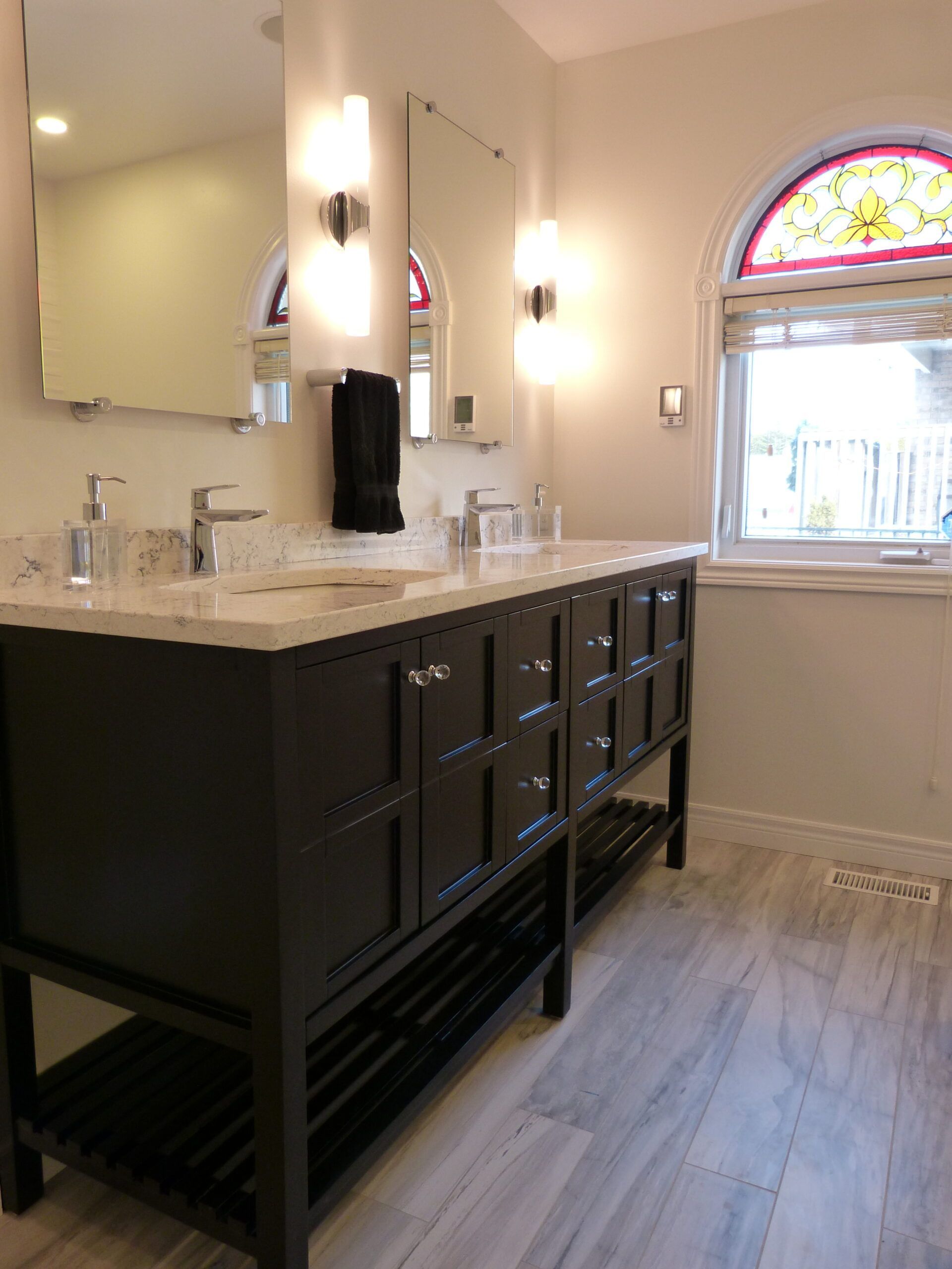 Bathroom with a dark brown vanity, two mirrors, and a stained-glass window.