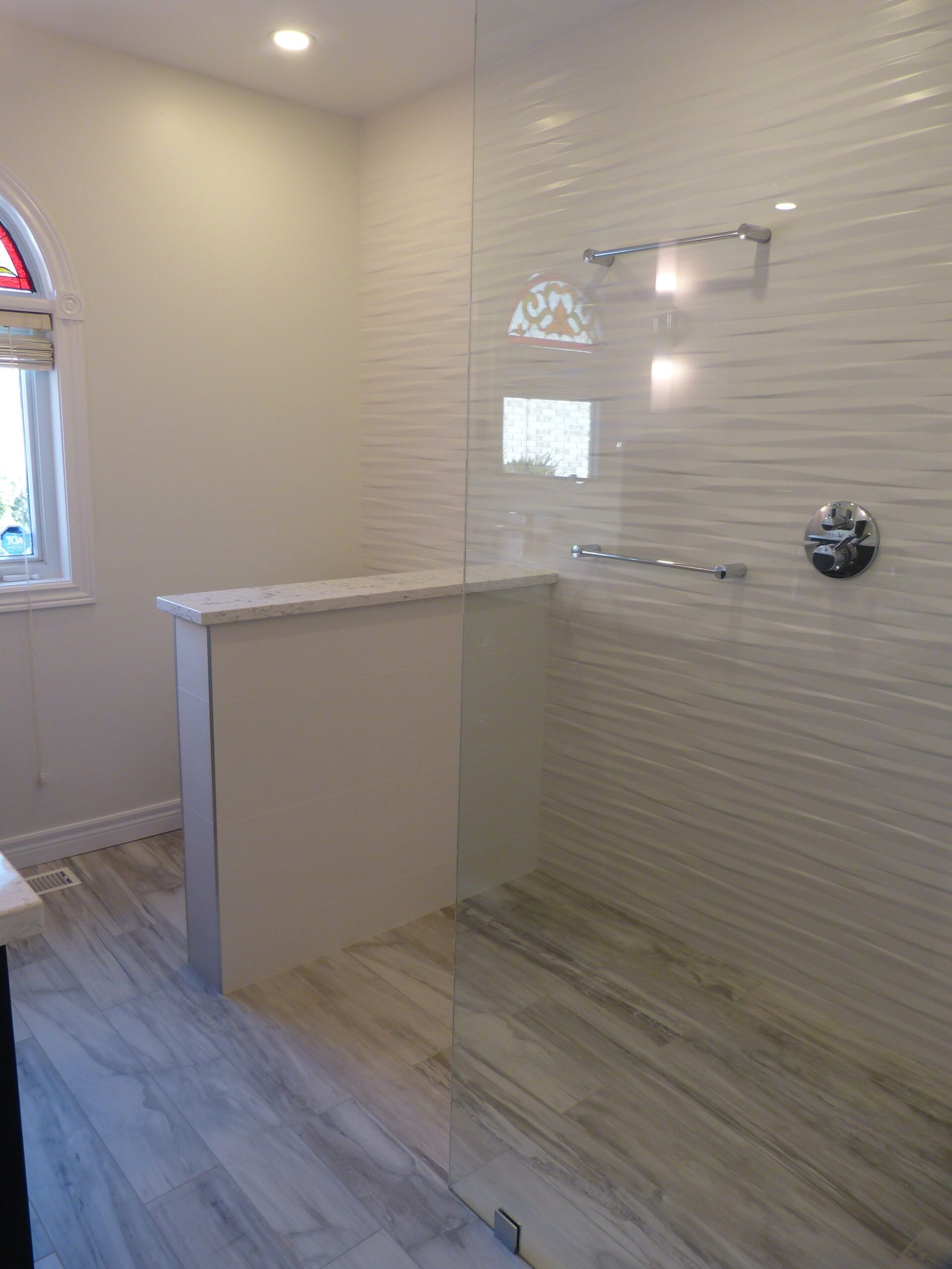 Modern bathroom with white textured wall, glass shower, and light wood-look floor.