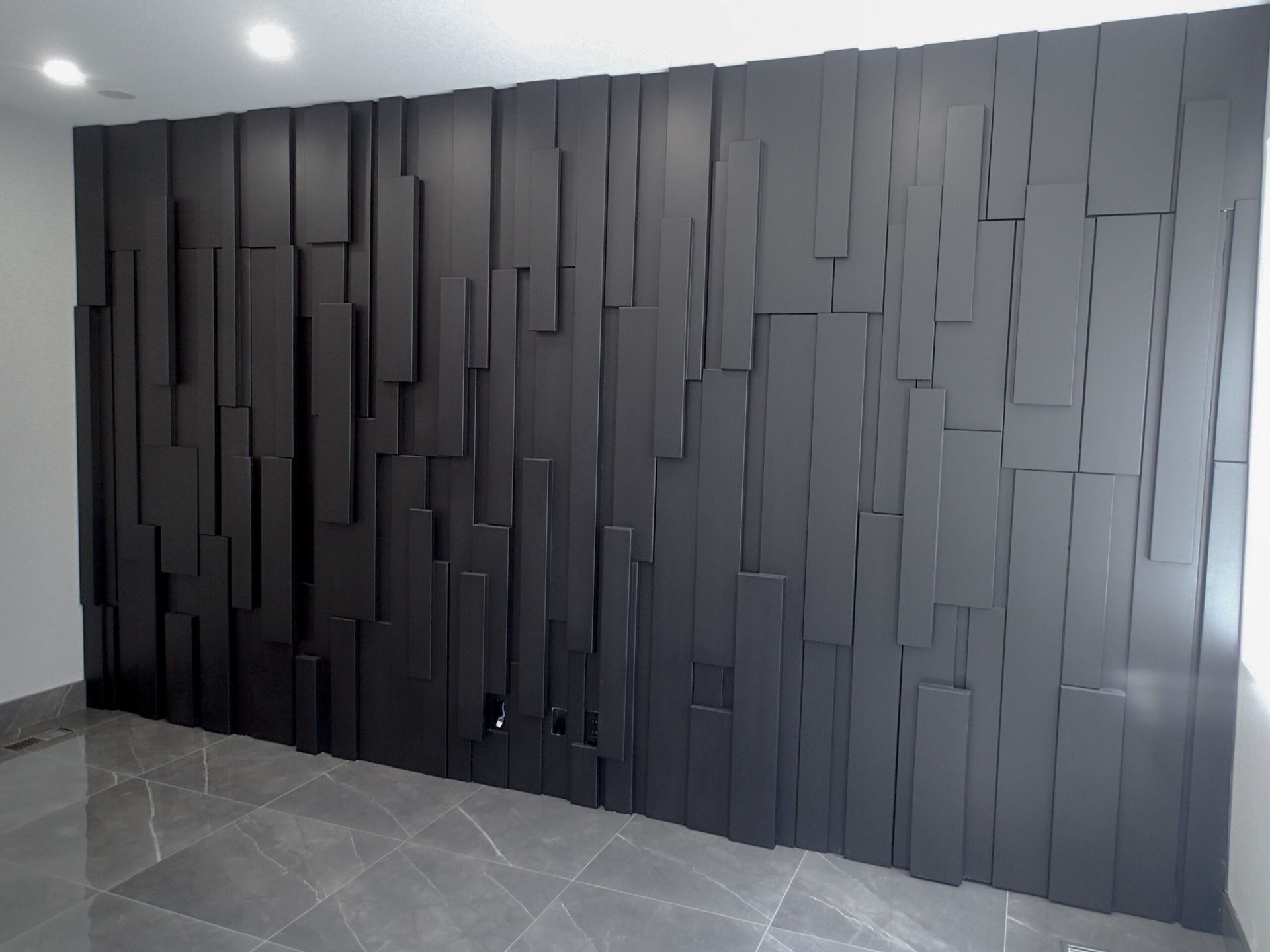 Black, textured wall made of vertical rectangular blocks. Interior setting, gray floor.