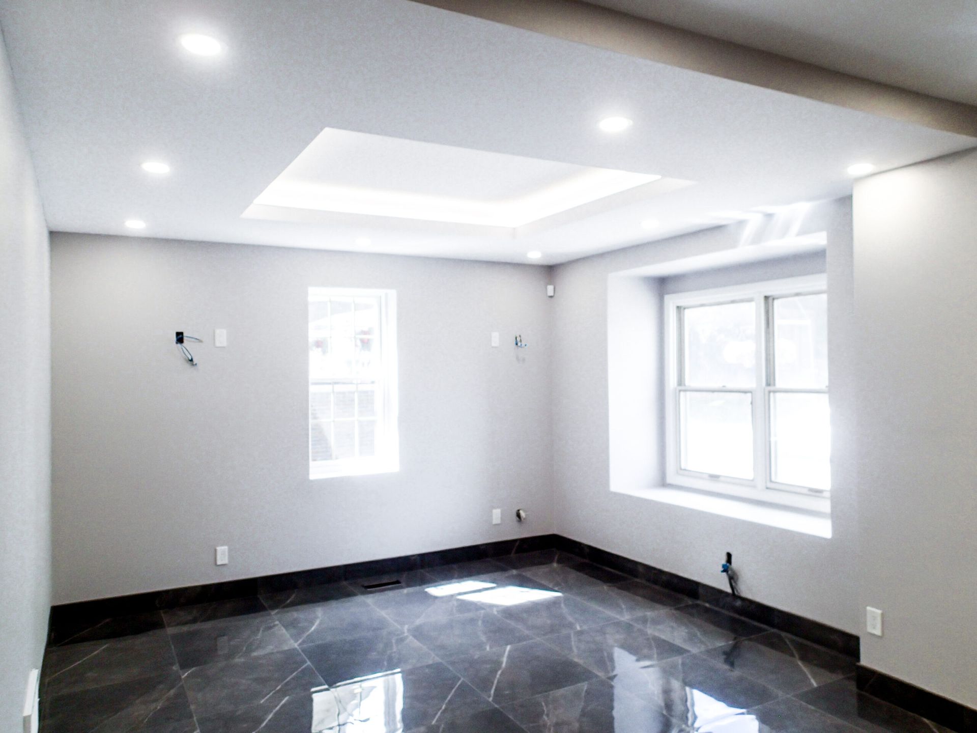 Empty room with gray walls, two windows, and a dark, shiny floor.