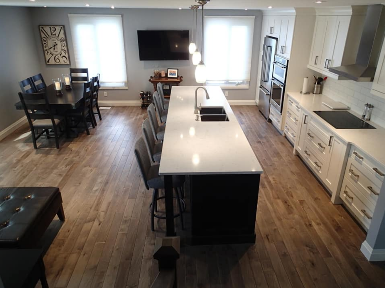 Open-concept kitchen with large island, dining table, light wood floors, and white cabinets.