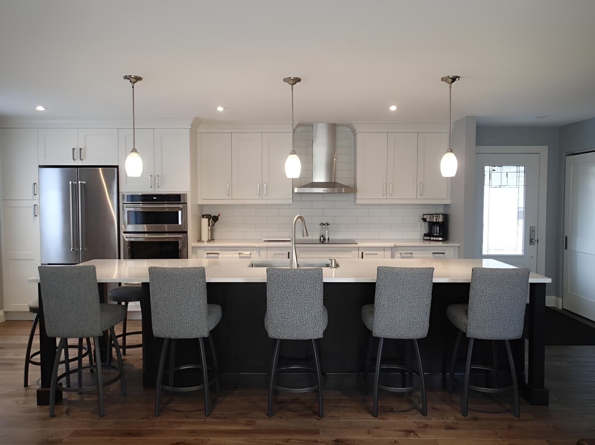 Modern kitchen with white cabinets, black island, stainless steel appliances, and gray bar stools.