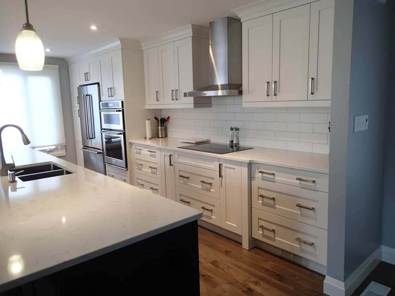 Modern white kitchen with stainless steel appliances, white countertops, and dark island.