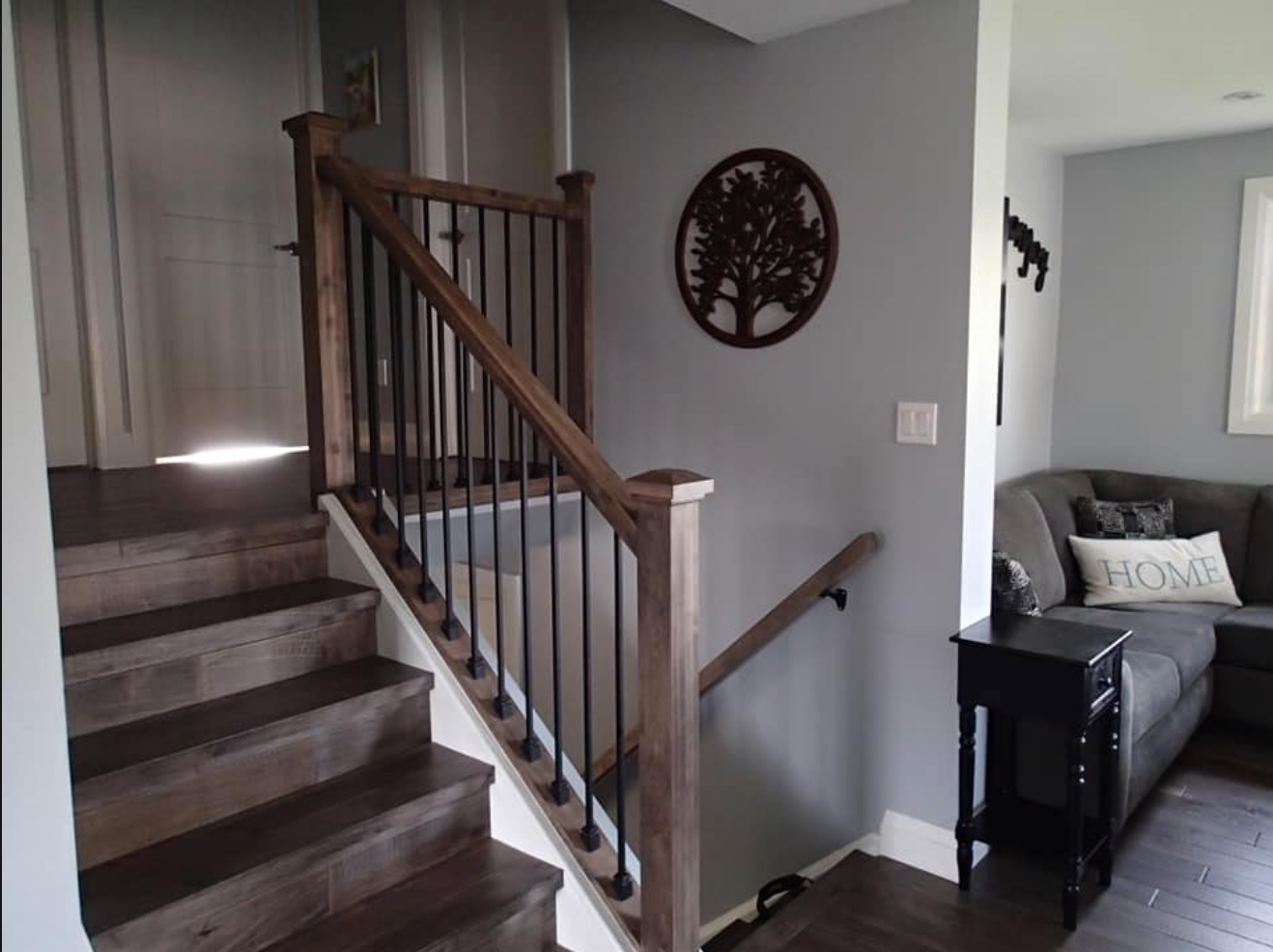 Staircase with wooden steps and railing, black metal spindles, and gray wall with decorative tree.