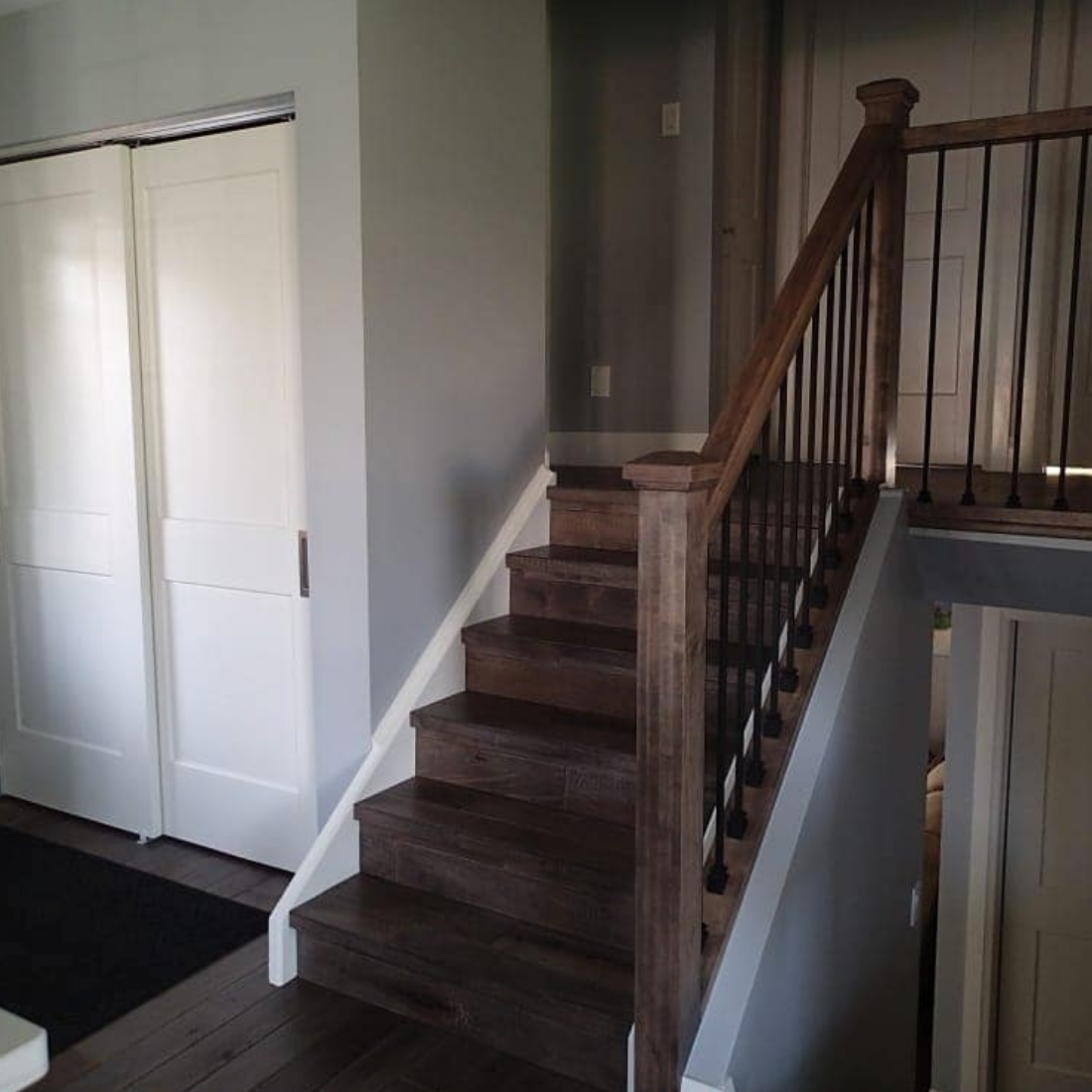 Staircase with wooden steps and railing, white doors, and gray walls.