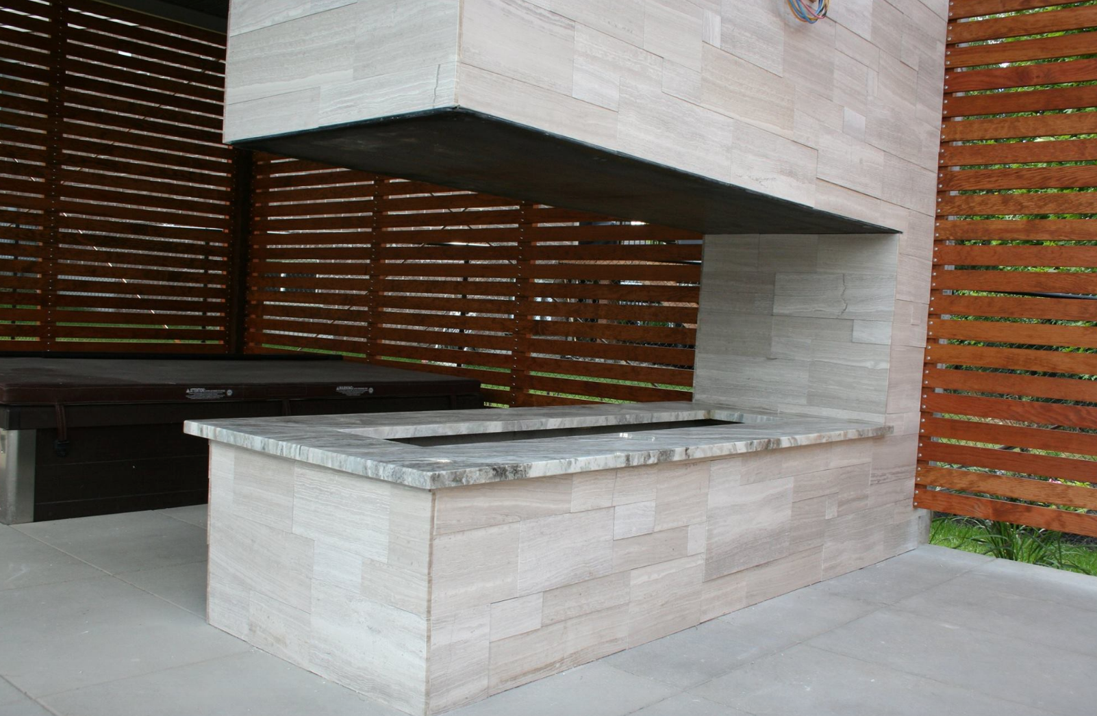 Outdoor fireplace with stone facade and granite countertop, set against a wooden fence.