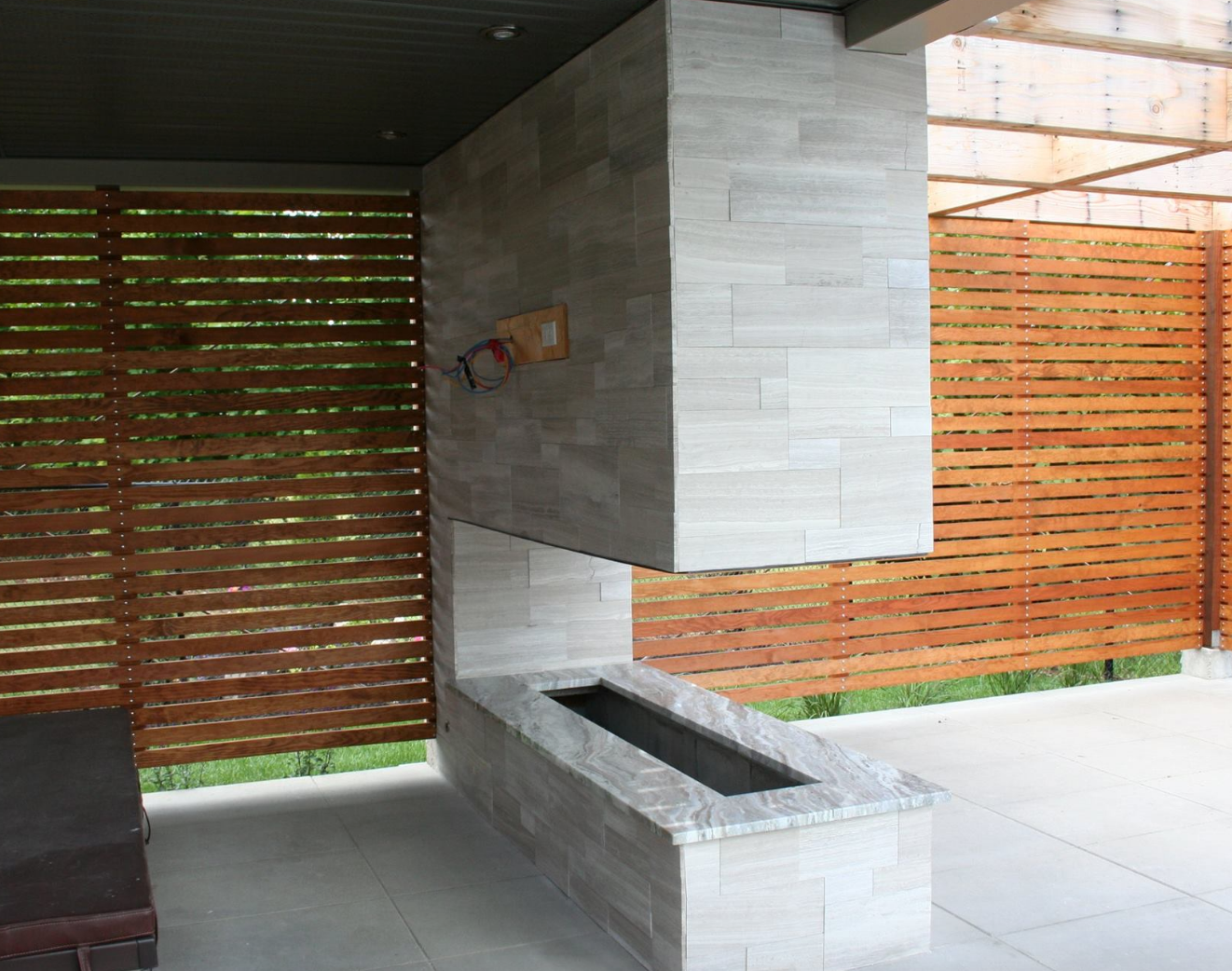 Outdoor fireplace with gray stone, surrounded by a wooden slat fence and a patio.