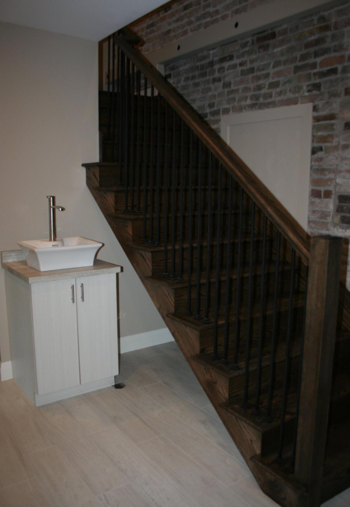 A staircase with dark wood and black spindles next to a white vanity sink and a brick wall.