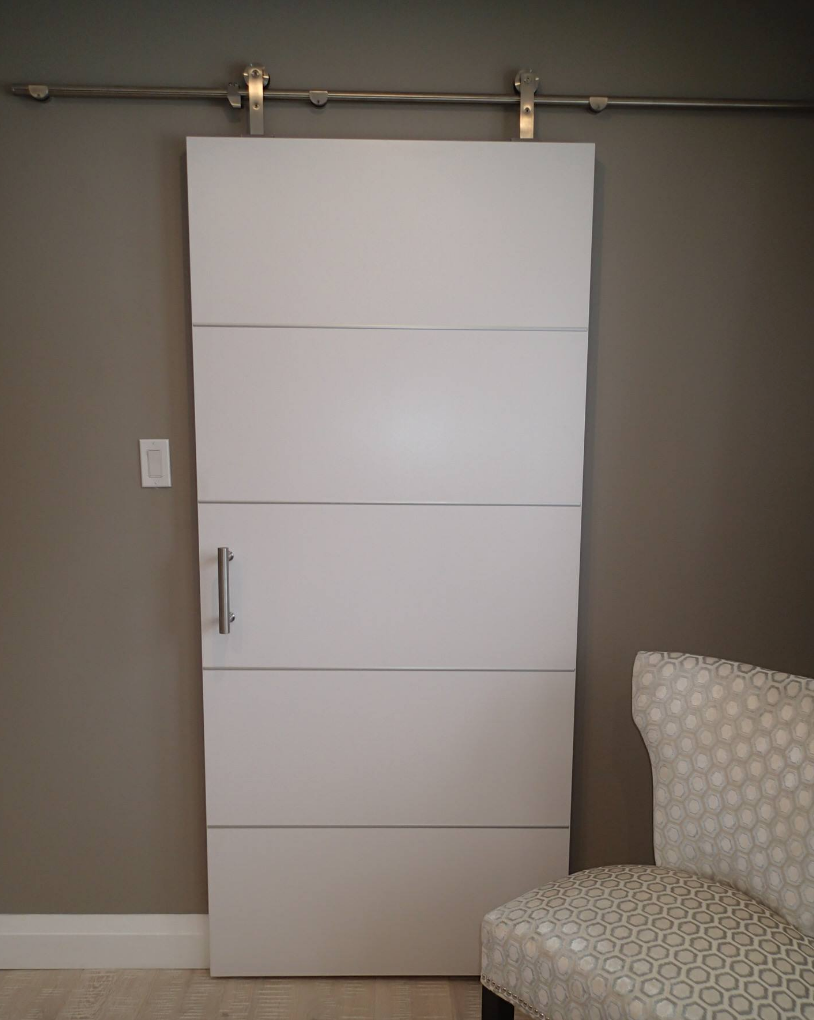 White sliding door on a gray wall with a silver handle, rail, and a patterned chair.