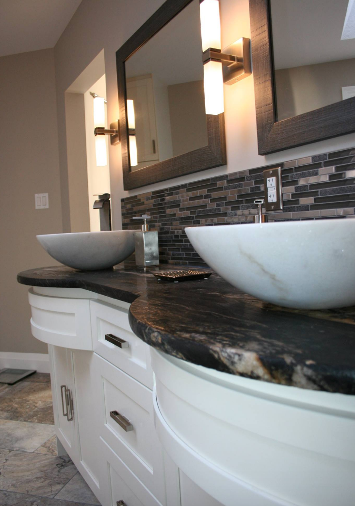 Bathroom vanity with curved white cabinets, vessel sinks, dark countertop, and a mosaic backsplash.