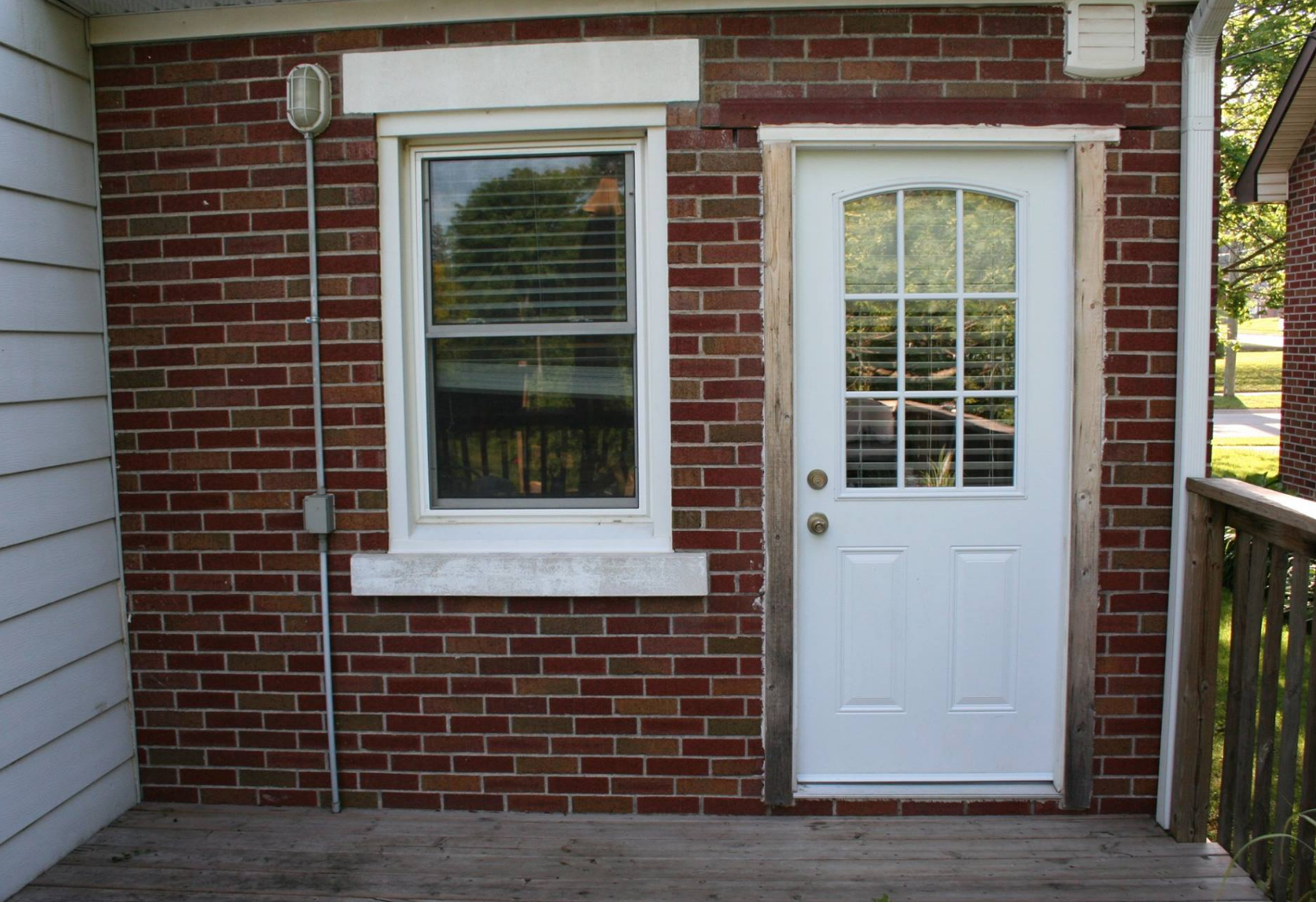 Brick exterior with white door and window. A porch with a railing is on the right.