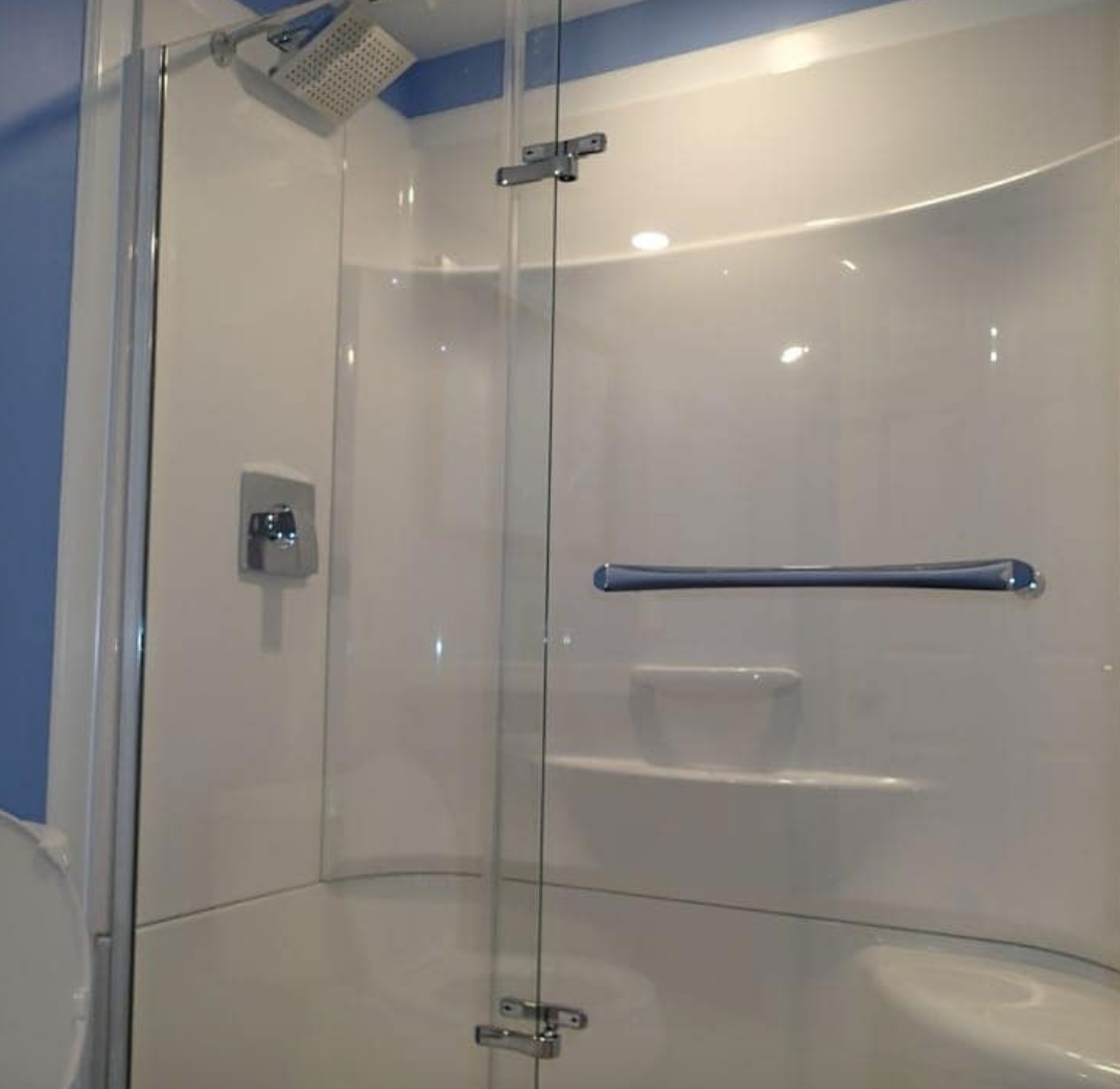 White shower stall with glass door, chrome fixtures, and blue wall.